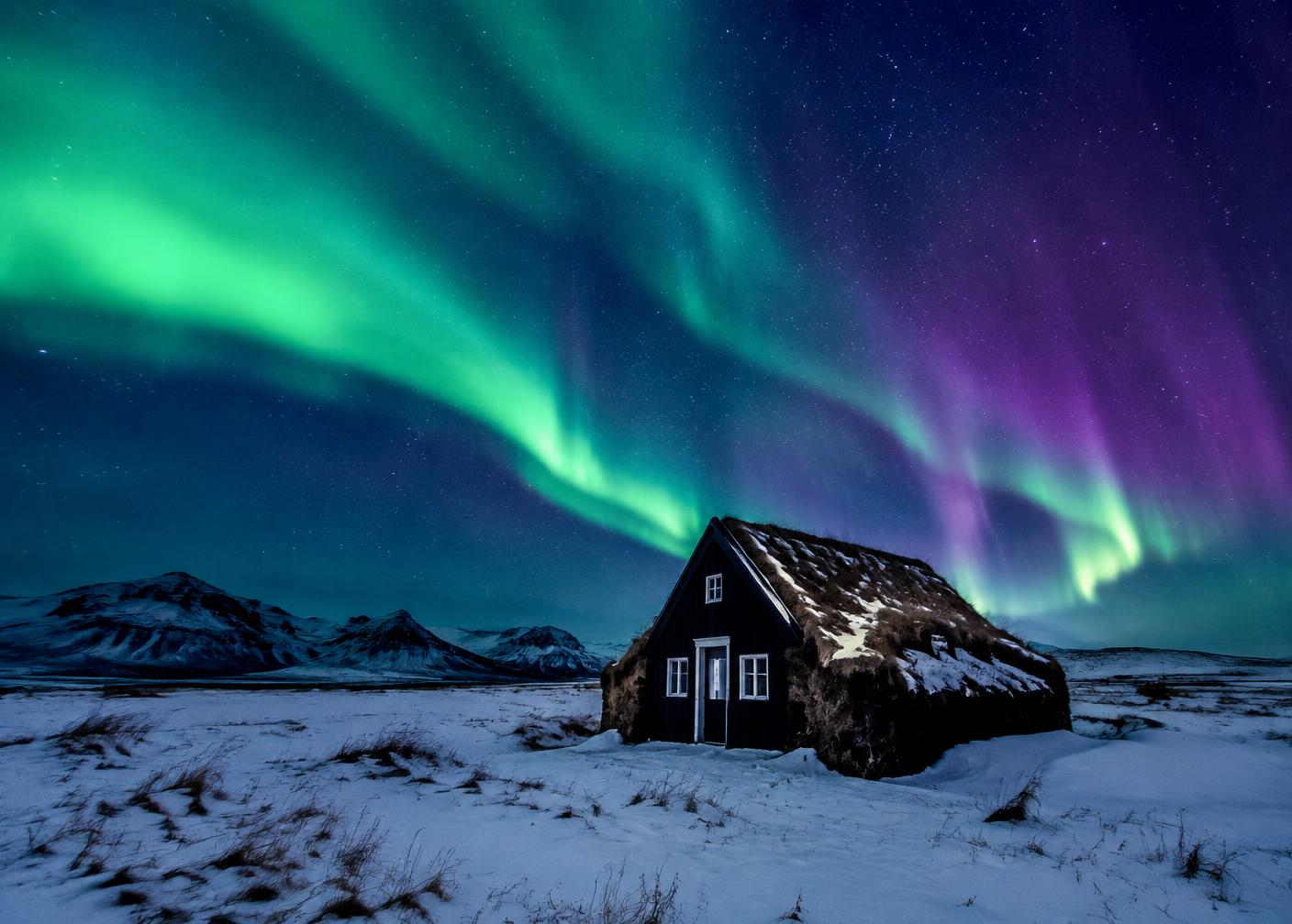 Northern lights above a turf-roofed Icelandic cabin in snow