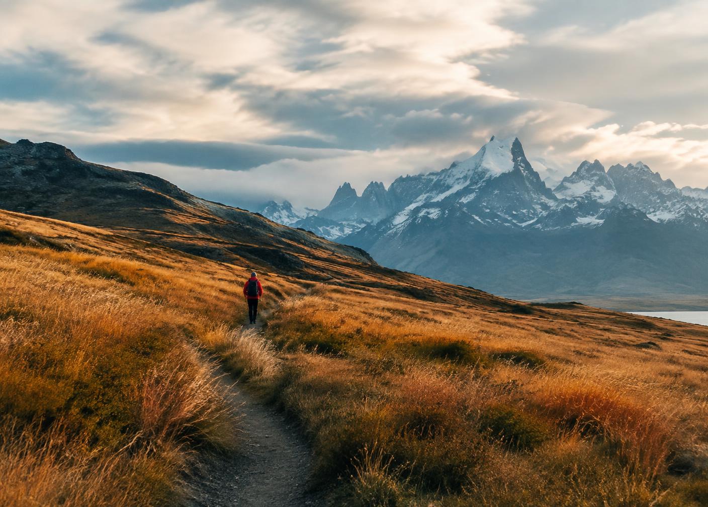 Hiker on a trail through golden Patagonian steppe below jagged mountains